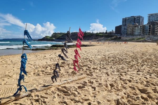 Colourful team bandanas tied to driftwood on a sunny beach as part of the Mini Beach Olympics setup by Pinnacle Team Events