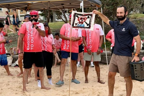 ABB team member holding up a hand-painted pirate flag with a Pinnacle Team Events facilitator on the beach during a Mini Beach Olympics team building event