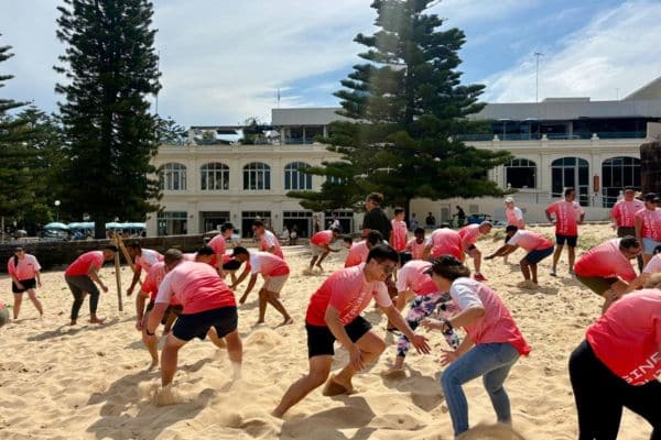 Large corporate group in matching pink t-shirts competing in a beach running activity during a Mini Beach Olympics team building event with Pinnacle Team Events