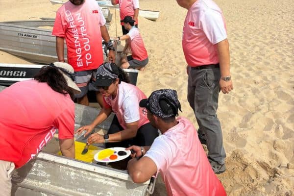 ABB team members painting a flag on the sand as part of a creative challenge during a Mini Beach Olympics outdoor team building event with Pinnacle Team Events