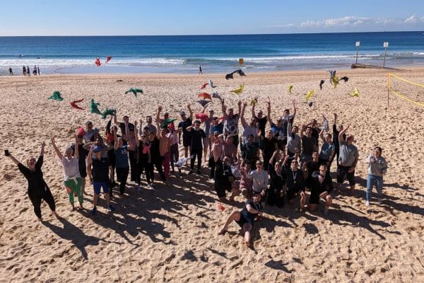 Large corporate group celebrating on the beach by throwing colourful bandanas in the air at the conclusion of a Pinnacle Team Events Mini Beach Olympics