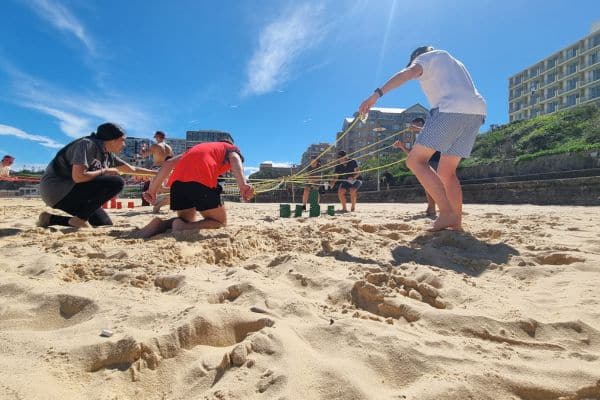 Corporate team using ropes to stack blocks on the sand during the Skyscrapers challenge at a Mini Beach Olympics event with Pinnacle Team Events