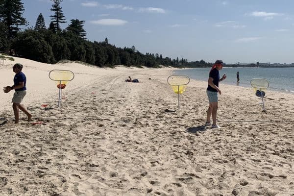 Corporate team members competing in a hoop target throwing challenge on the beach during a Pinnacle Team Events Mini Beach Olympics activity
