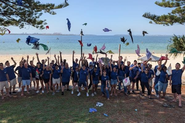 Large corporate team celebrating on a beachside lawn by throwing colourful bandanas in the air at the end of a Pinnacle Team Events Mini Beach Olympics