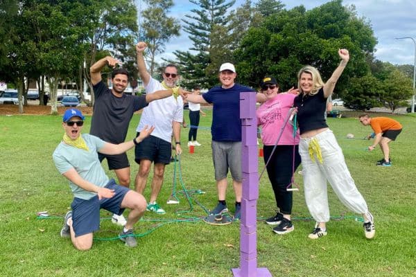 Corporate team celebrating after completing the Skyscrapers block stacking challenge on grass during a Mini Olympics outdoor team building event with Pinnacle Team Events