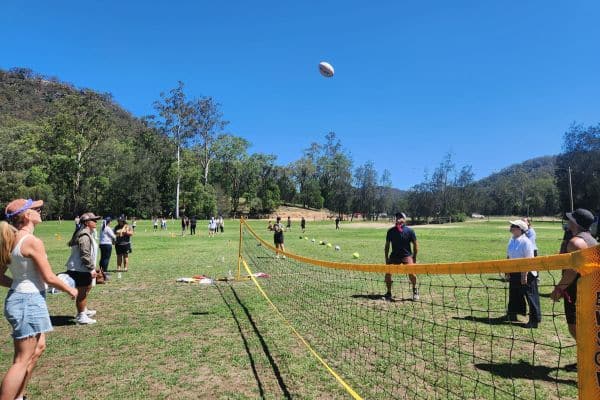 Corporate teams playing volleyball on grass surrounded by bushland during a Mini Olympics outdoor team building event with Pinnacle Team Events