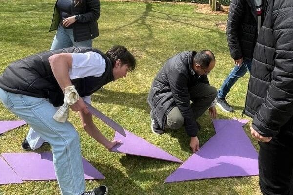 PTE Scramble CIB Accountants 2024 Team members assembling large purple tangram puzzle pieces on a lawn during The Scramble team building activity