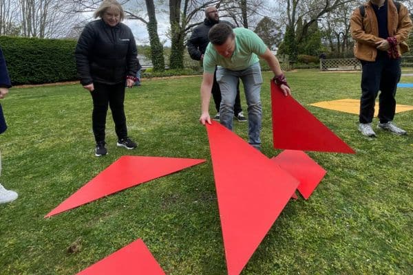 Team member assembling large red tangram puzzle pieces on a lawn during The Scramble team building activity
