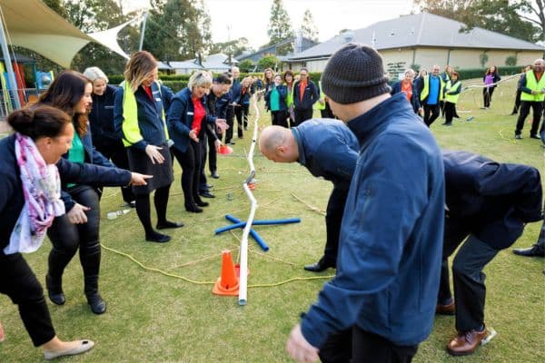 Large group of participants collaborating to guide a ball through a PVC pipe pipeline during the Project Pipeline outdoor team building activity