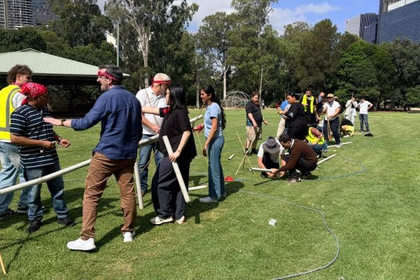 Teams working together to assemble a PVC pipe pipeline structure on a city park lawn during the Project Pipeline outdoor team building activity