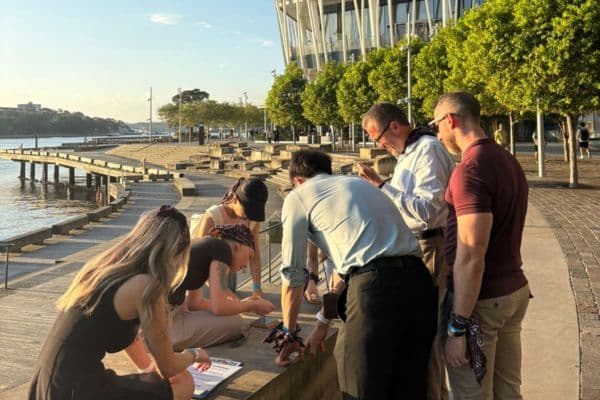 Corporate team solving clues along a waterfront promenade at sunset during a Ransom outdoor team building activity with Pinnacle Team Events