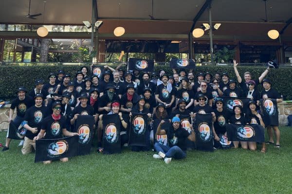 Large corporate team in matching black t-shirts holding Ransom event flags for a group photo at the conclusion of a Pinnacle Team Events outdoor team building day