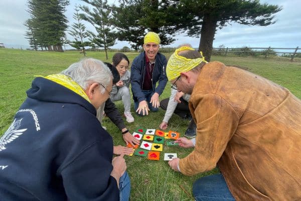 Four team members on grass wearing yellow bandanas solving a playing card tile puzzle during The Scramble