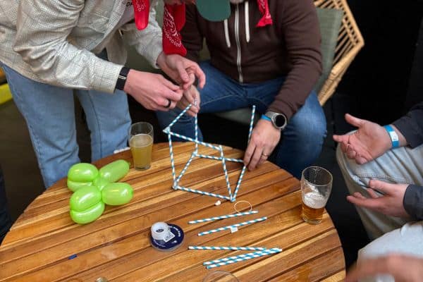 Team members constructing a geometric shape using striped straws at a pub table during The Scramble