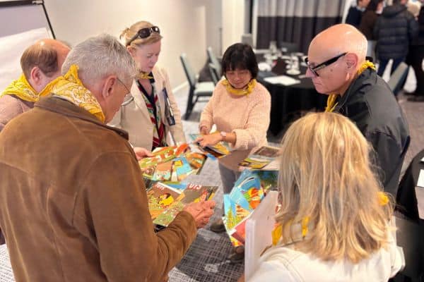 Group of participants in yellow scarves reviewing puzzle cards around a table during an indoor Scramble team building session