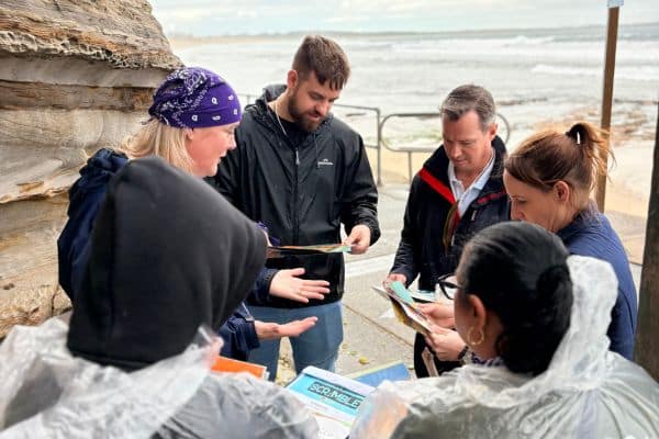 Small team reviewing Scramble activity cards at a coastal location on an overcast day