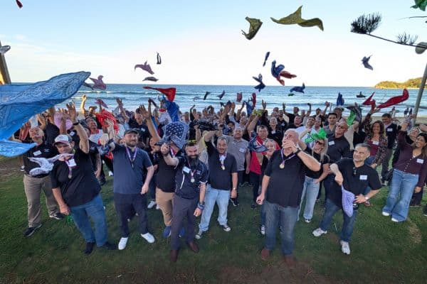 Large group celebrating at the end of The Scramble by throwing colourful bandanas in the air at a beachfront location