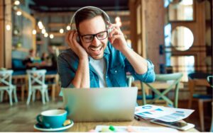 man smiling with headphones looking at his laptop computer