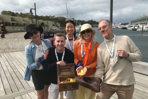Viatris team members wearing winner medals and posing together on a sunny beachfront after completing a Pinnacle Team Events Treasure Hunt
