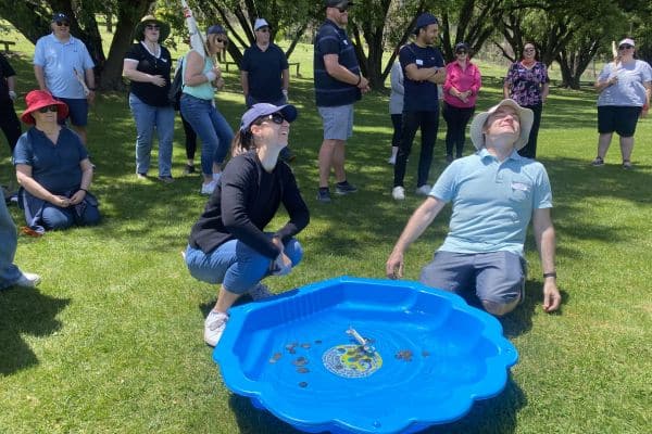 Corporate participants reacting with laughter during a paddling pool treasure retrieval challenge at a Pinnacle Team Events Treasure Hunt