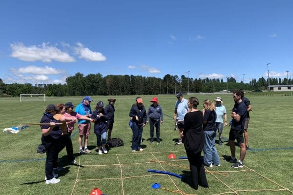 Corporate team gathered on a sports field receiving instructions during a Treasure Hunt outdoor team building event with Pinnacle Team Events