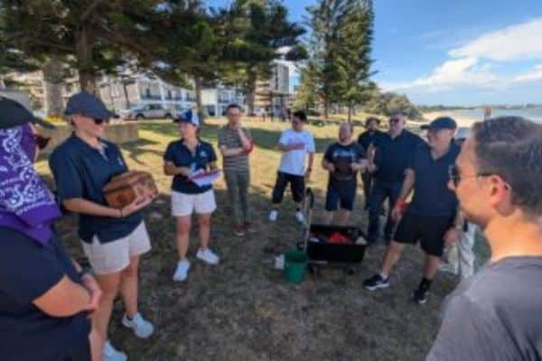 Pinnacle Team Events facilitator briefing the Viatris team beside a coastal park at the start of an outdoor Treasure Hunt team building activity