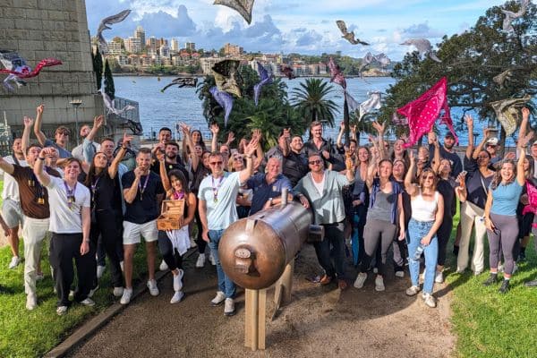 Large corporate group celebrating beside a historic cannon at Sydney Harbour after completing a Pinnacle Team Events Treasure Hunt outdoor team building even