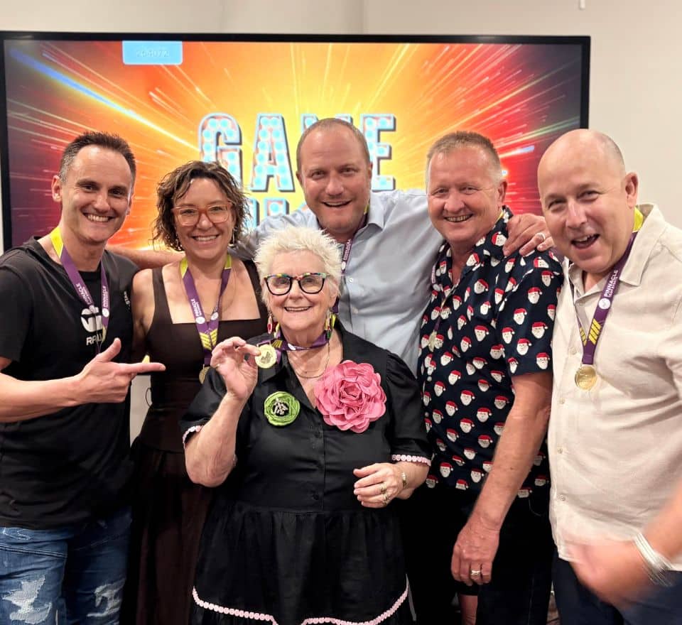 Group od people standing infront of TV screen inside, happy and holding up medals